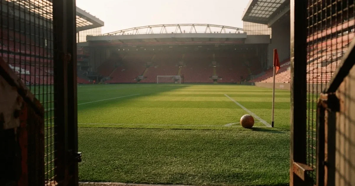 Blick durch ein Stadiontor auf einen grünen Rasen im Abendlicht, ein Ball ruht an der Eckfahne, die Tribünen sind leer.