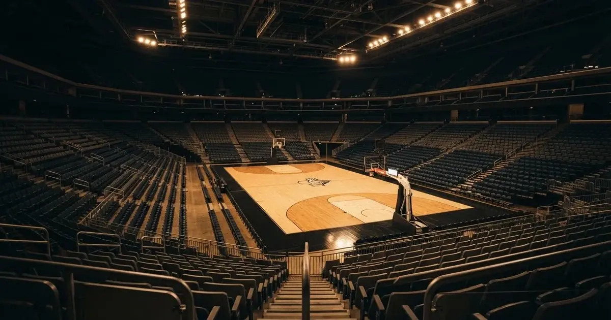 Eine leere Basketballhalle von einer oberen Tribünenreihe aus gesehen, Parkett und Körbe im Licht der Hallenstrahler.